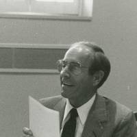 Richard DeVos sitting at a table holding a stack of papers.